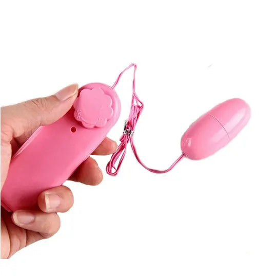 Hand holding pink wired remote control with connected oval pink vibrating egg on white background