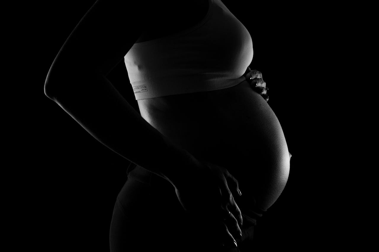 about-us Captivating grayscale close-up of a pregnant woman highlighting a baby bump, conveying anticipation and love.